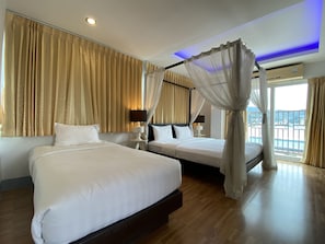 A hotel room with two beds, a balcony, and a view of the cityscape.