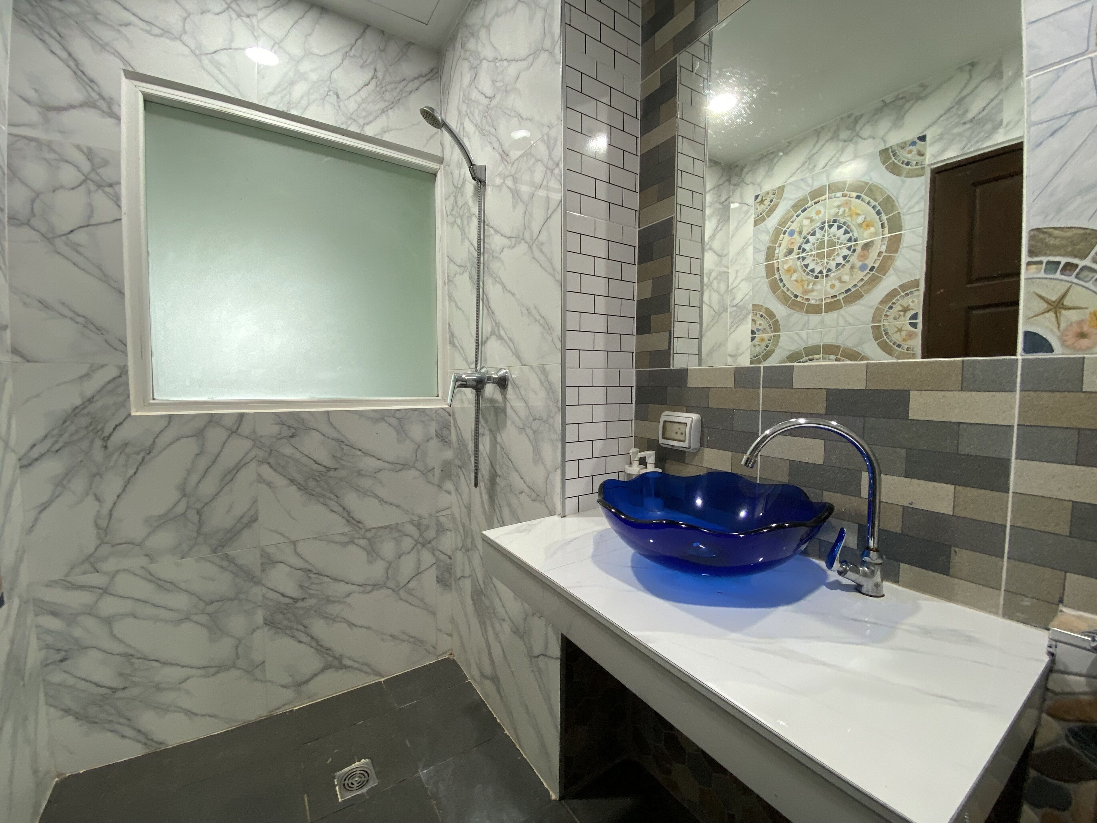 A bathroom with a marble wall, a blue glass sink, and a shower.
