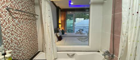 Un baño con bañera, ducha y vistas a un balcón con mobiliario exterior.