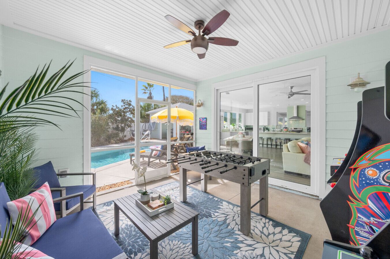 A room with a foosball table, a ceiling fan, and a view of a pool and outdoor seating area.