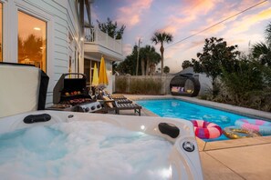 A backyard with a hot tub, a barbecue grill, lounge chairs, and a swimming pool.