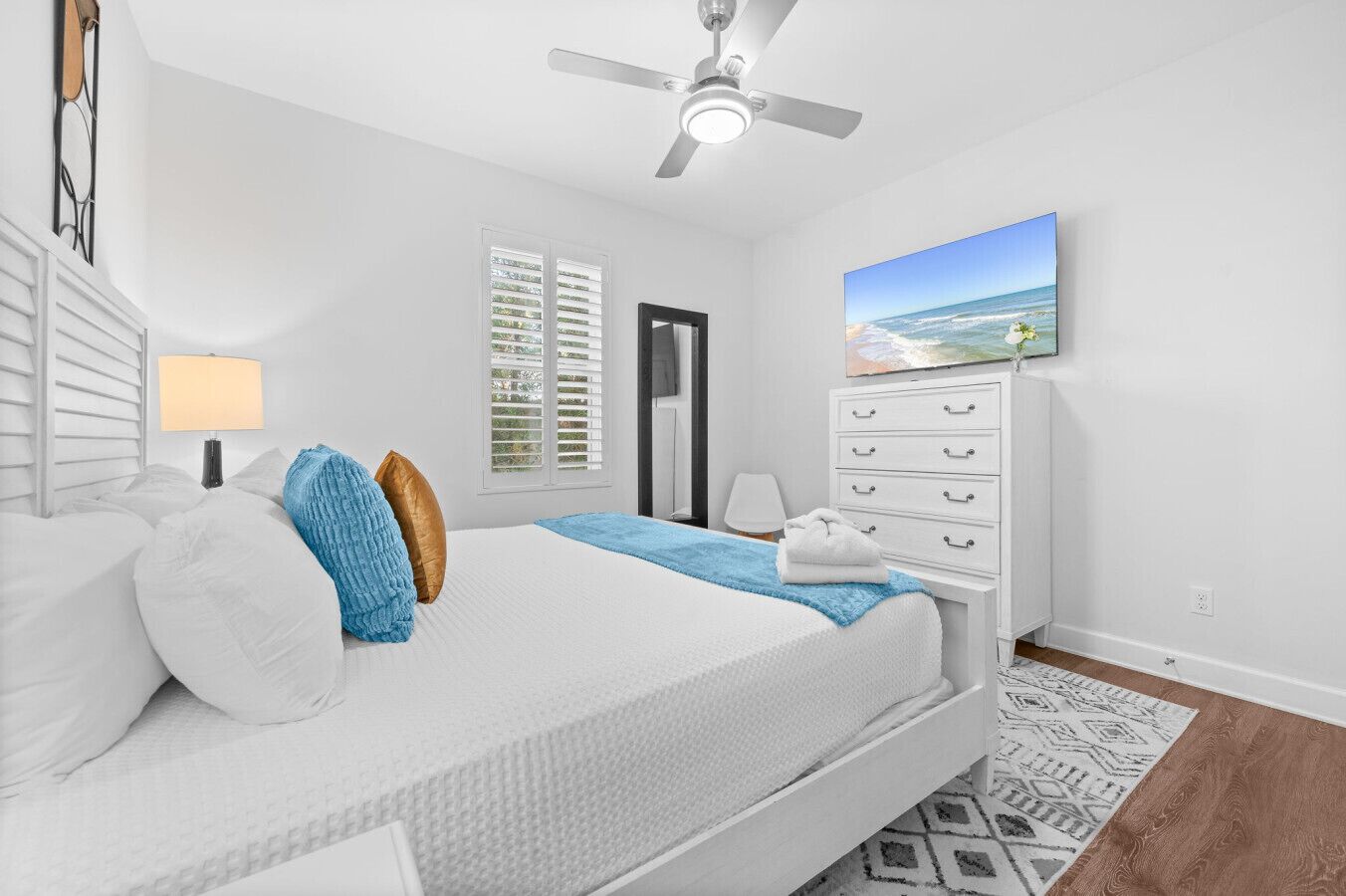 Een slaapkamer met een bed, een plafondventilator, een televisie, een dressoir en een raam met jaloezieën.