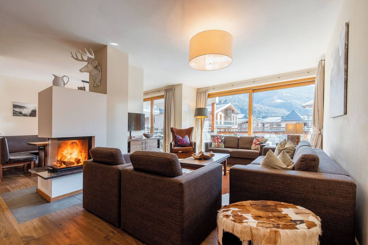Una sala de estar acogedora con chimenea, asientos cómodos y vistas a montañas.