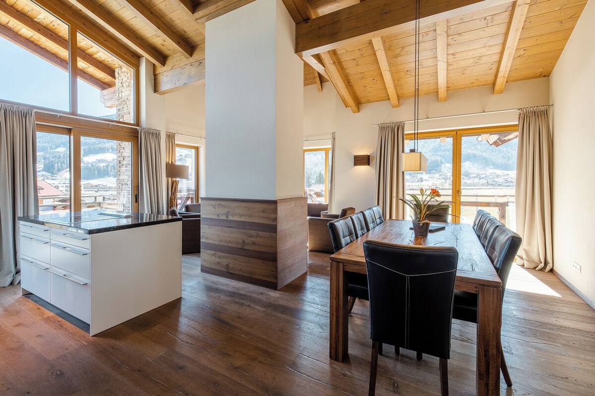 Un amplio comedor con una mesa y sillas de madera, ventanas grandes con cortinas, y vistas a un paisaje nevado.