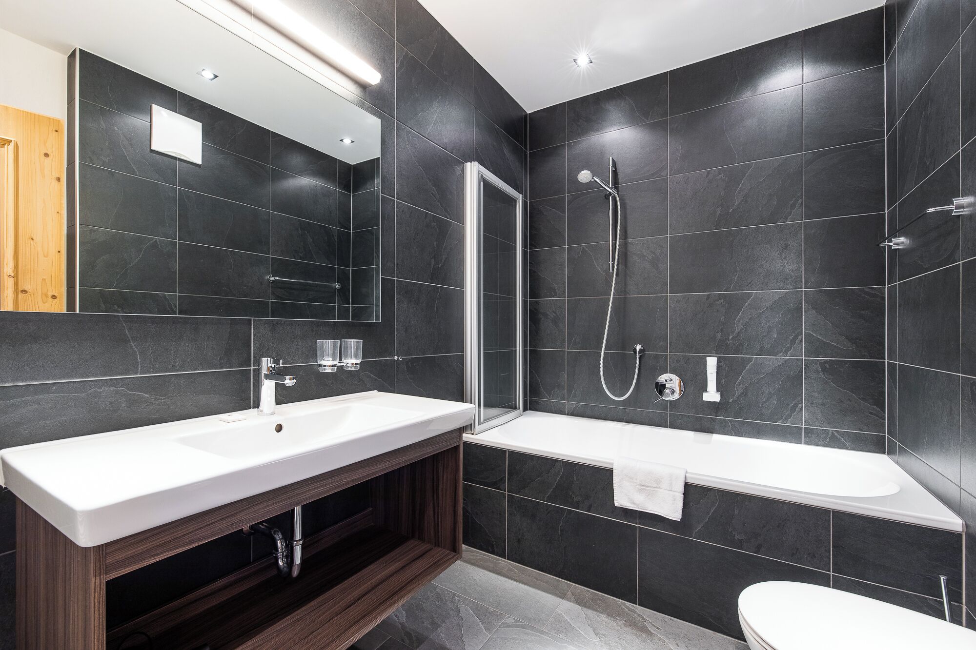 Un baño moderno con un espejo grande, un lavabo blanco, una bañera y una ducha.