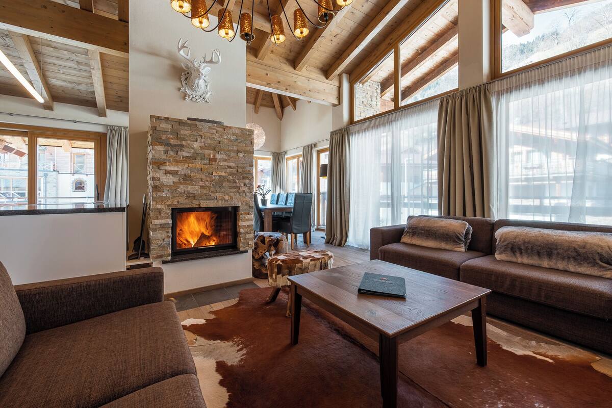 Una sala de estar acogedora con chimenea de piedra, vigas de madera y ventanas grandes.