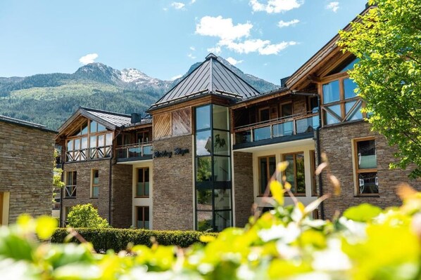 Un hôtel moderne avec une façade en pierre, de grandes fenêtres et une vue sur les montagnes en toile de fond.