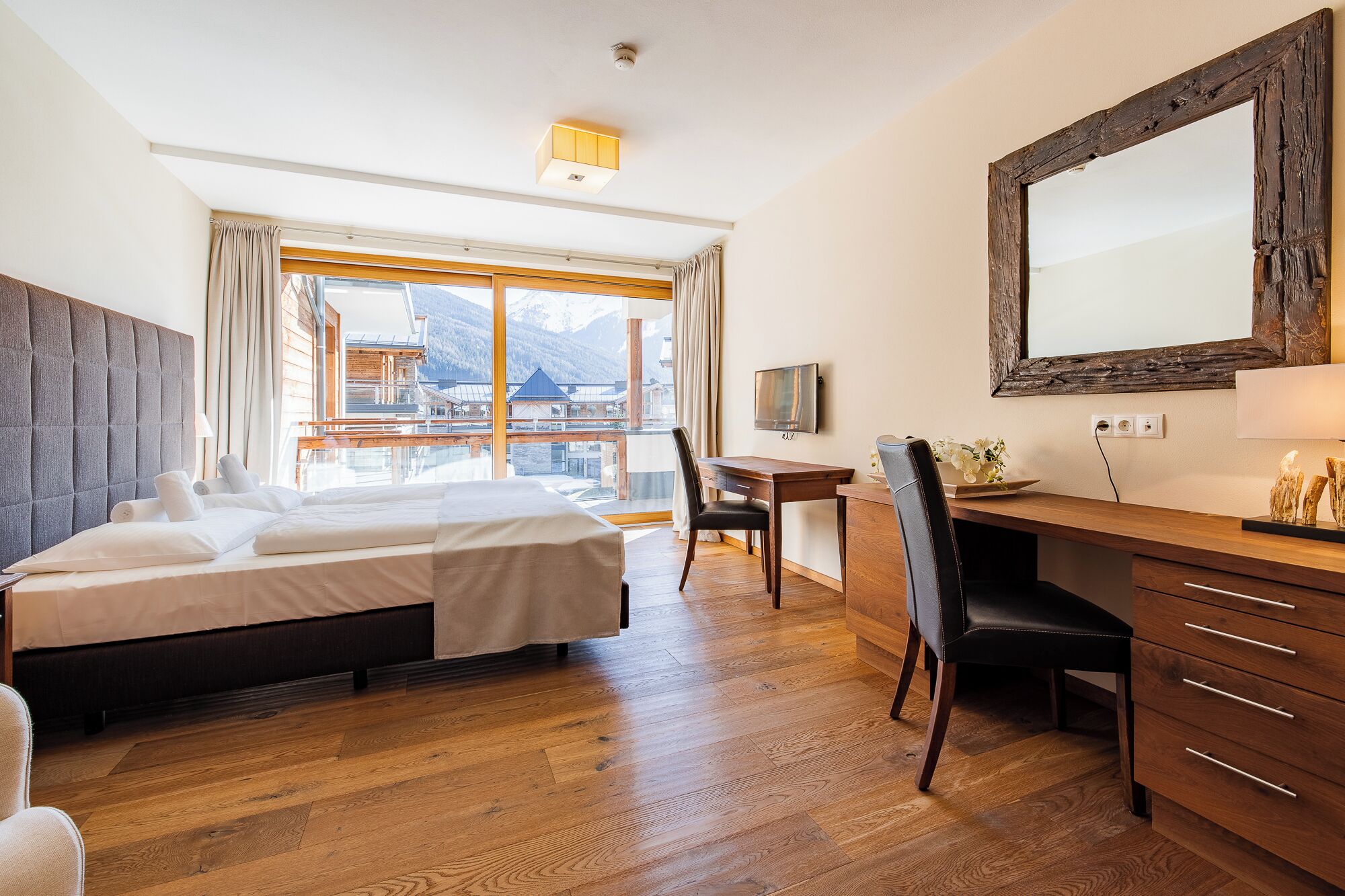 Une chambre d’hôtel équipée d’un lit, d’un bureau, d’une chaise et d’une grande fenêtre donnant sur les montagnes.