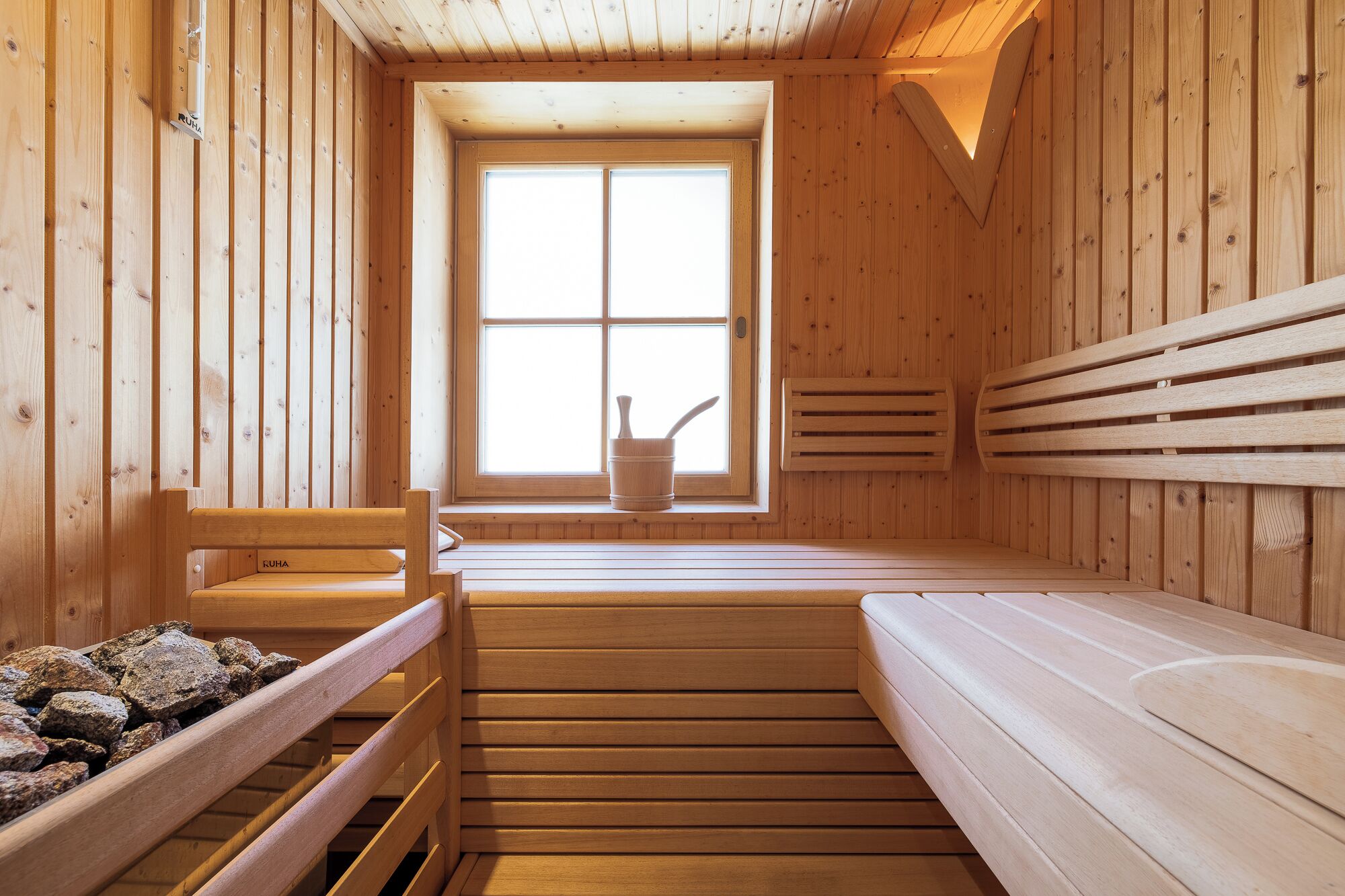 Una sala de sauna con bancos de madera, una ventana y una pileta de piedra.