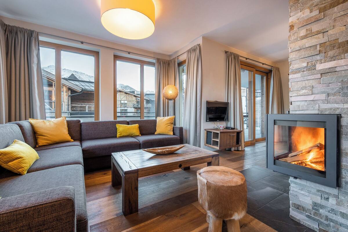 Una sala de estar moderna con un sofá seccional, una mesa de centro de madera, una chimenea de piedra y un televisor.