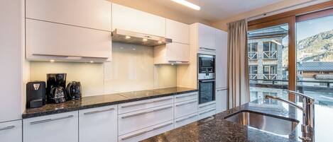 Una cocina moderna con armarios blancos, encimera de granito, horno empotrado y vistas a un paisaje montañoso a través de un amplio ventanal.