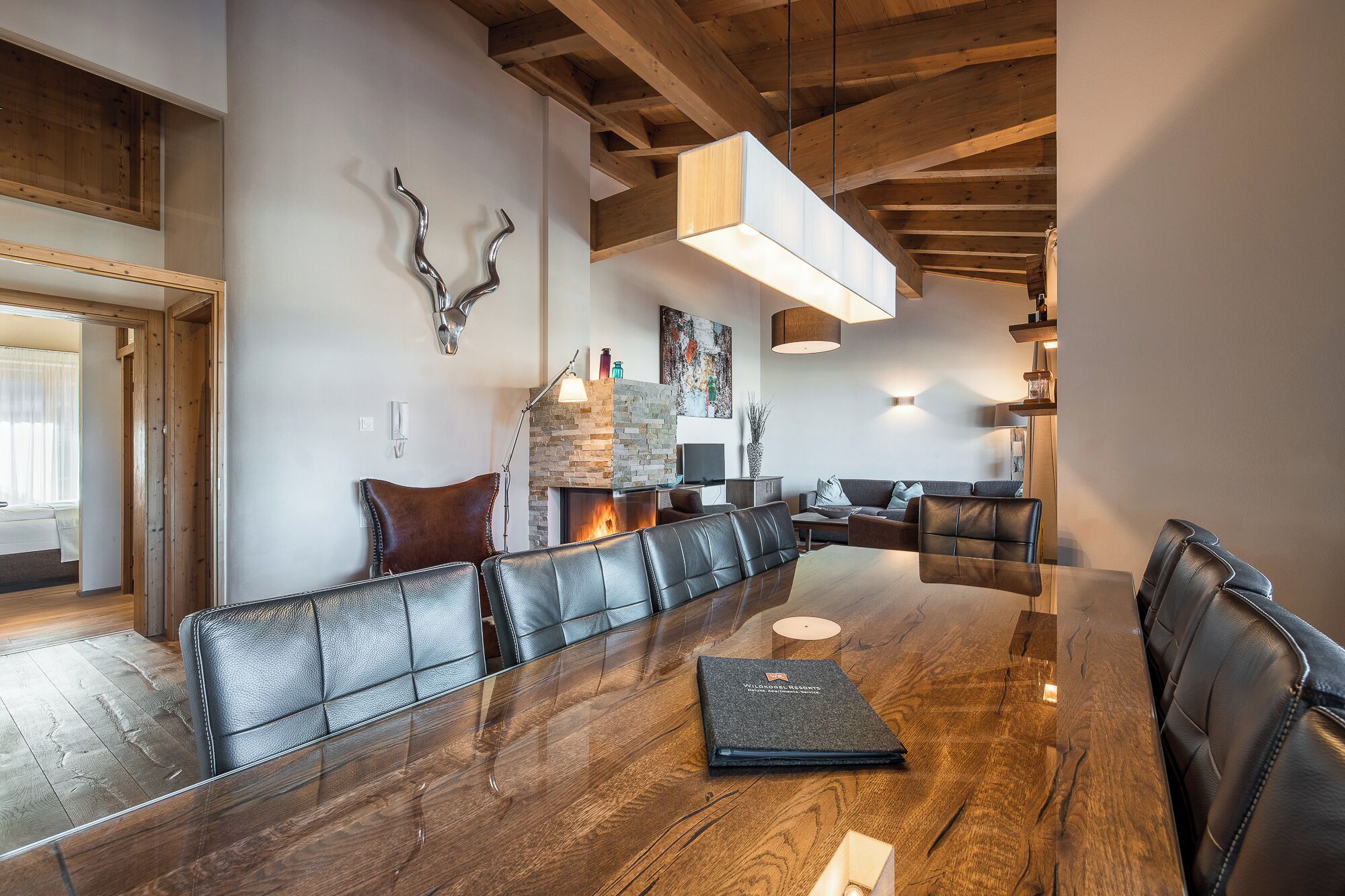 A modern dining area with a long wooden table, leather seating, and a stone fireplace.