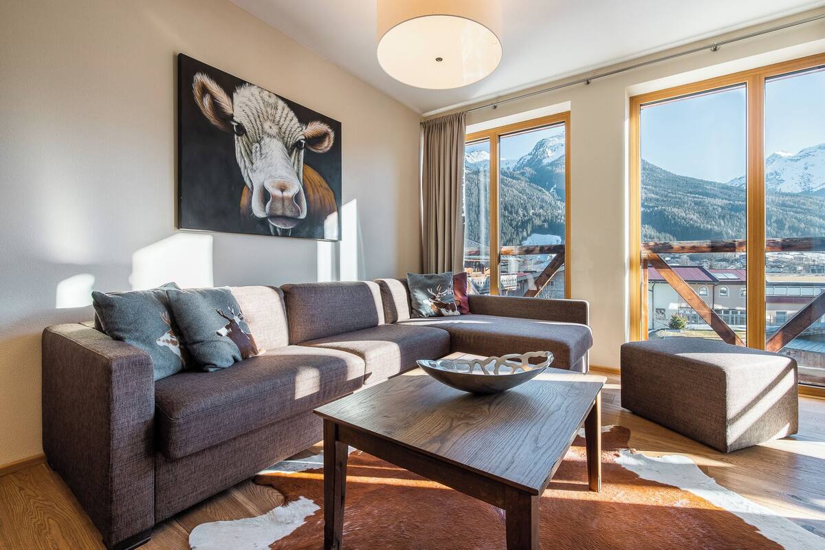 Una sala de estar moderna con un sofá modular, una mesa de centro de madera y un ventanal con vistas a la montaña.