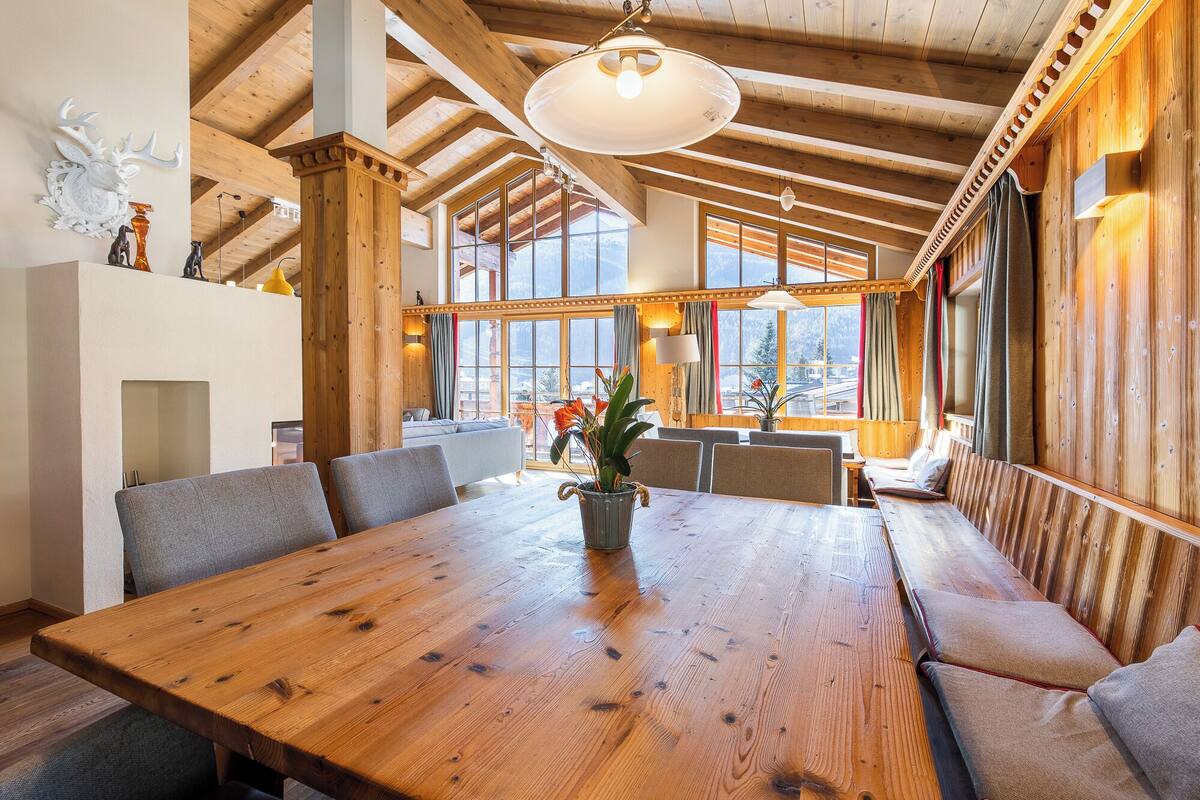 Un comedor de madera con una mesa grande, bancos y vistas a montañas a través de amplios ventanales.