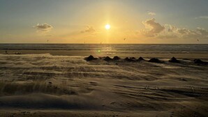 Una spiaggia con il sole che tramonta all'orizzonte, mare calmo e alcune persone in lontananza.