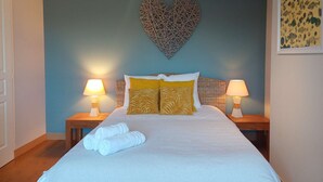 Un letto rifatto con lenzuola bianche, due comodini con lampade e un cuore decorativo sulla parete.