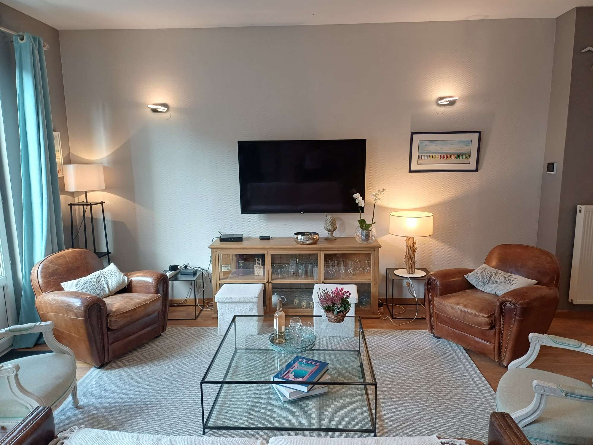 Una sala de estar con sillones de cuero, una mesa de centro de vidrio, un televisor de pantalla plana y un mueble con puertas de cristal.
