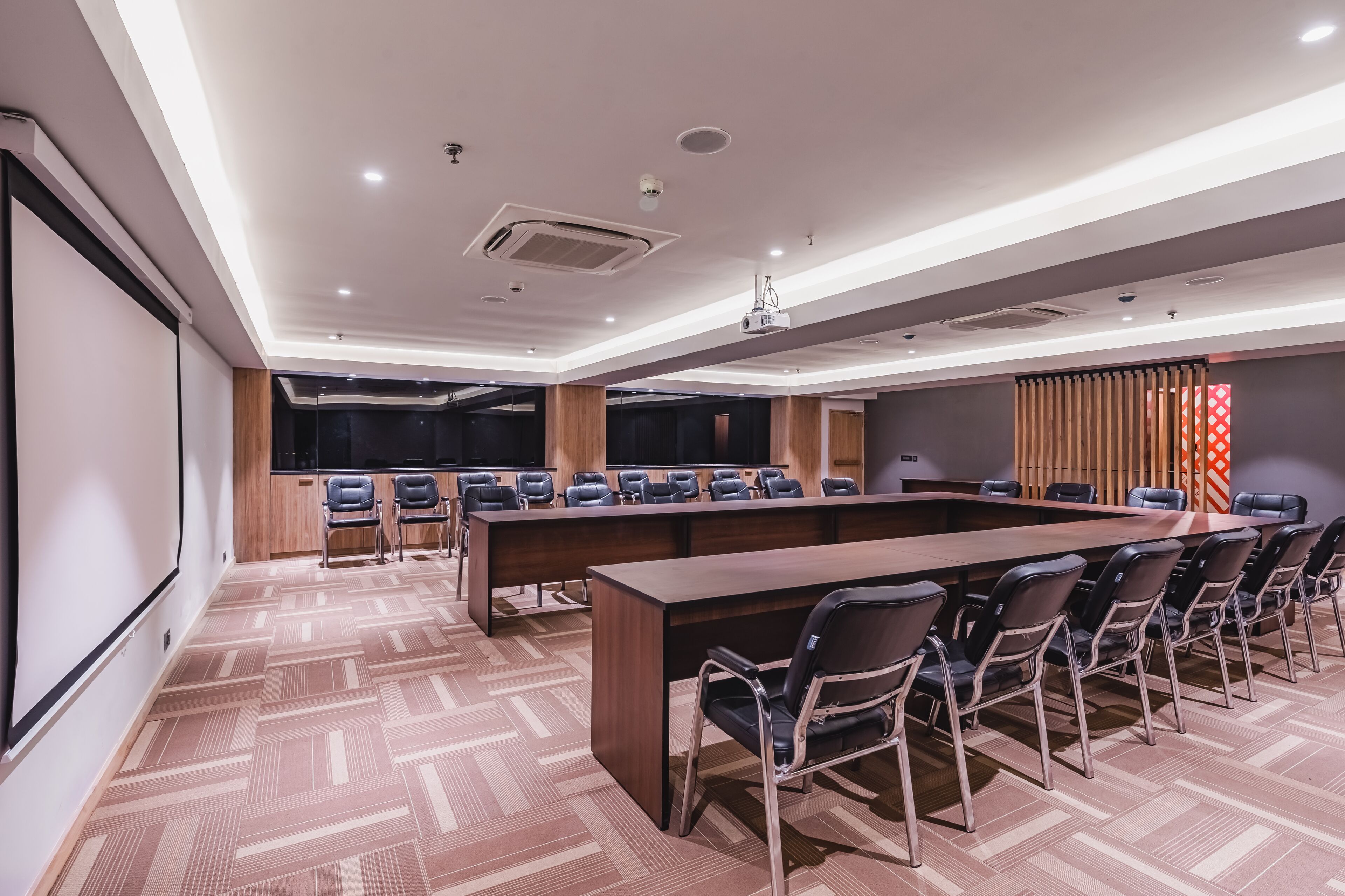 Ein Konferenzraum mit einem langen Tisch, Stühlen, einer Projektionsleinwand und Holzboden.