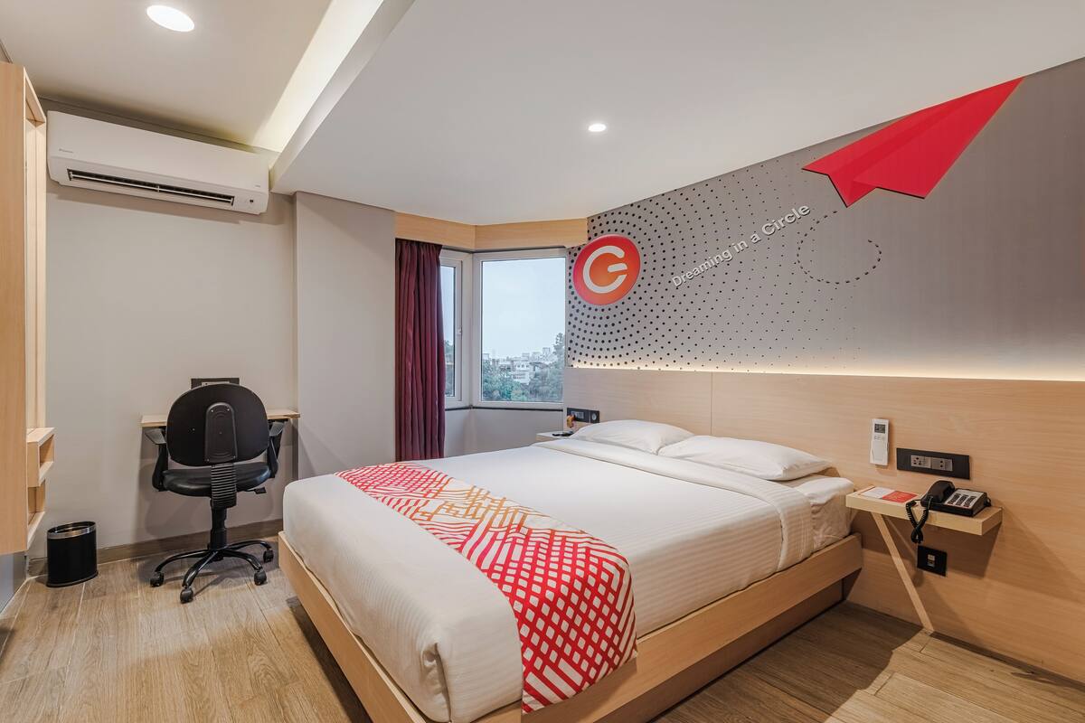 A hotel room with a bed, a desk, a chair, a window, and a wall decoration.