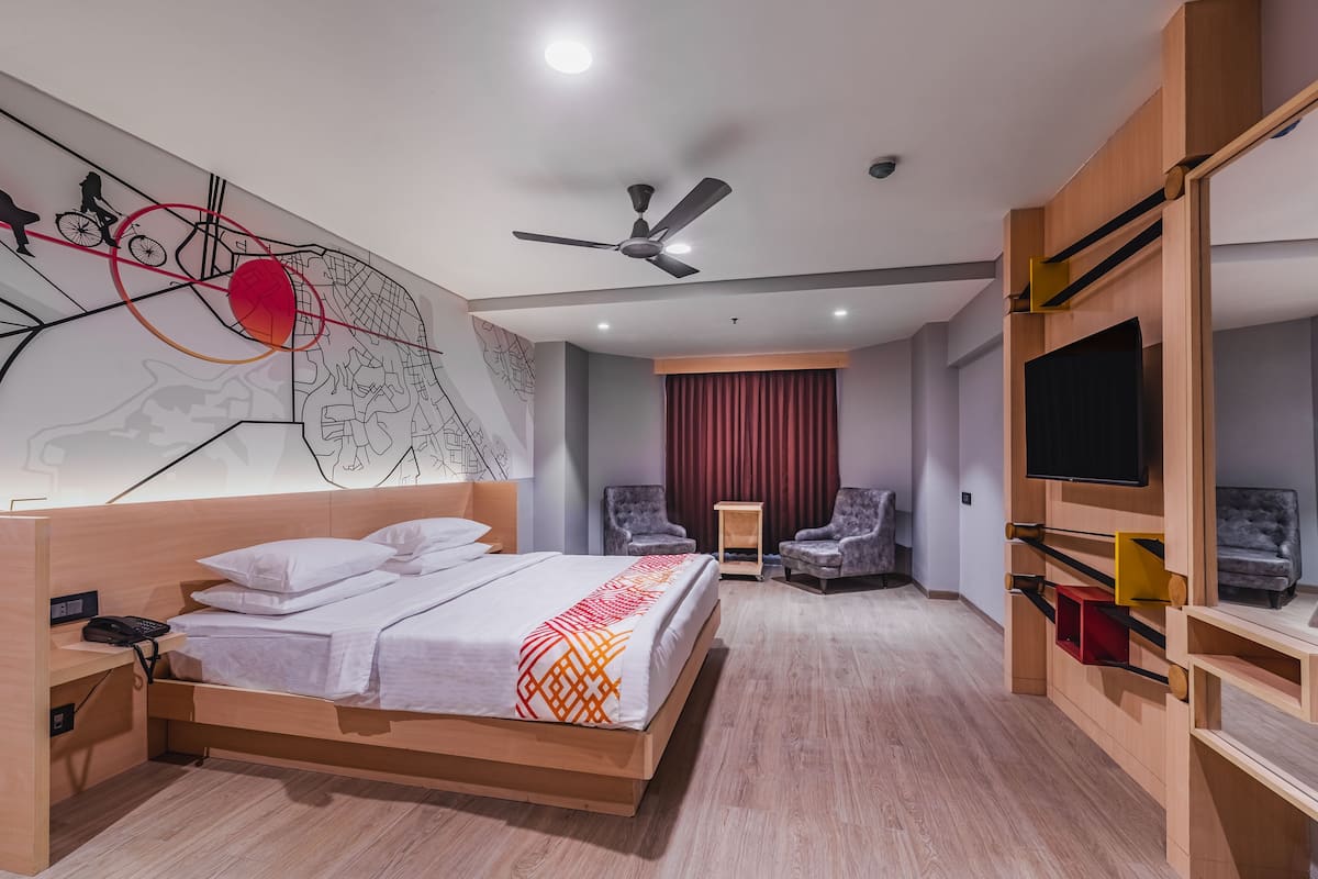 A hotel room with a bed, a ceiling fan, a TV, two armchairs, and a red curtain.