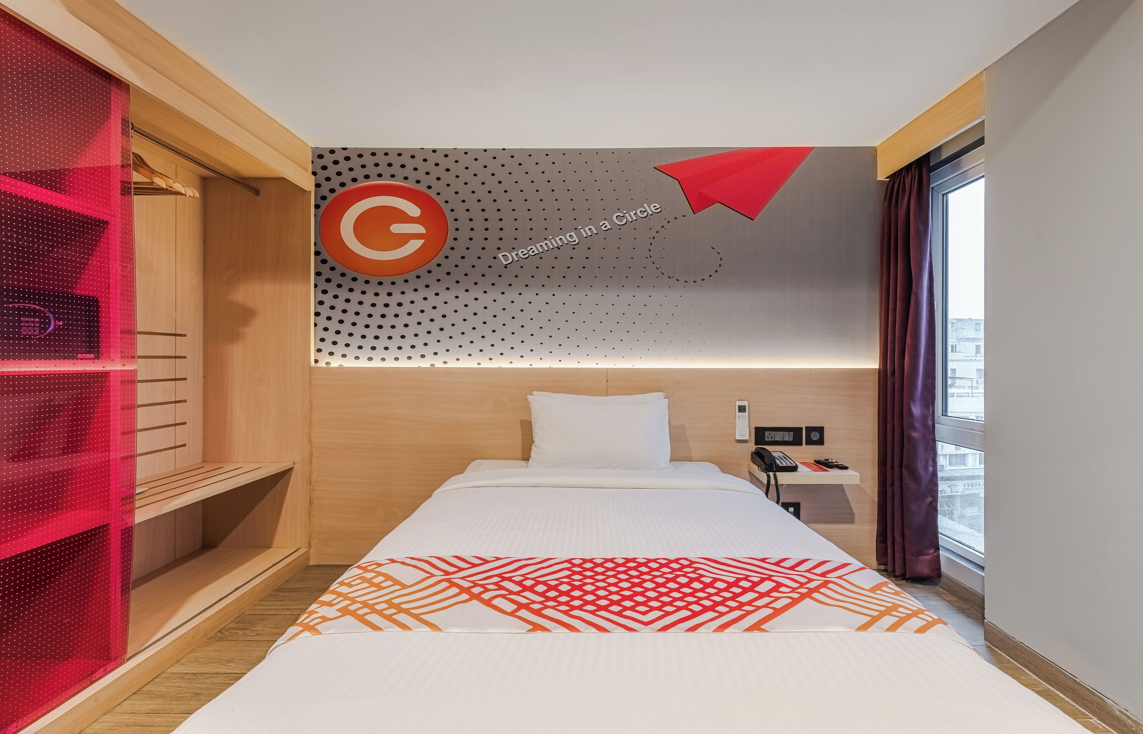 Habitación de hotel con cama, mesita de noche, teléfono y ventana con cortinas.