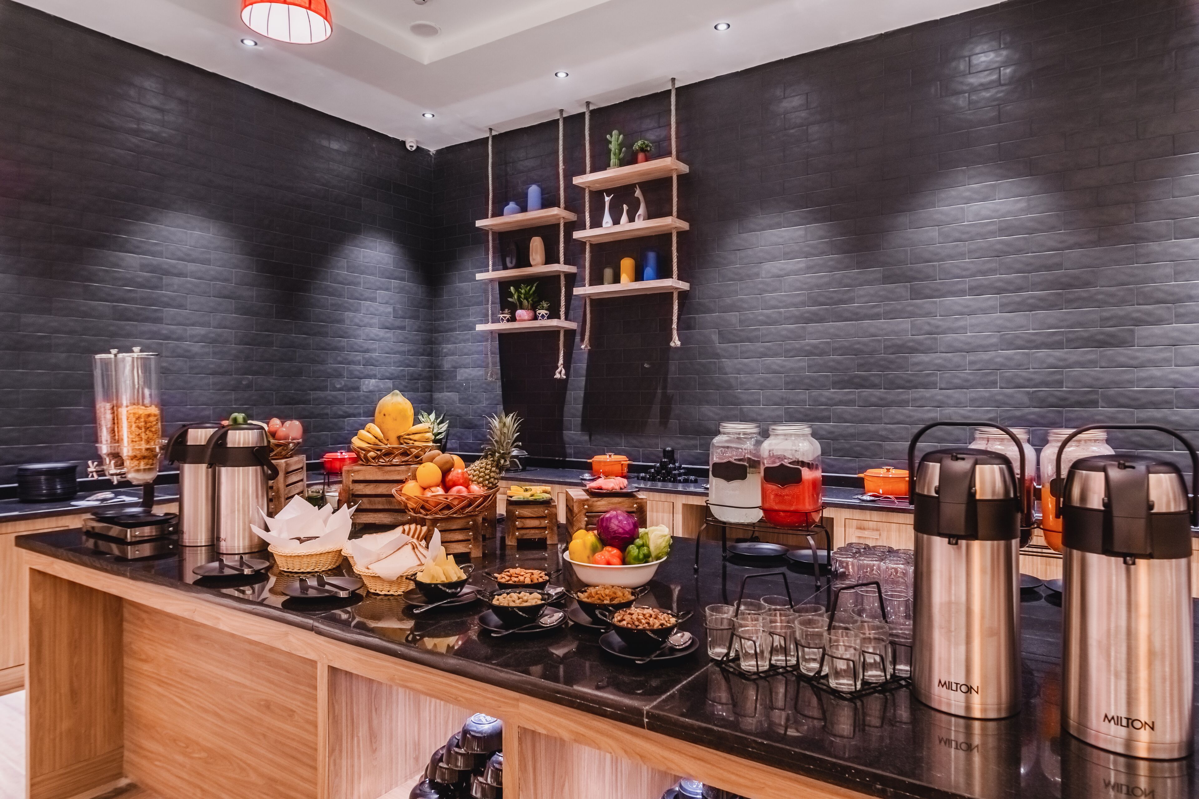Una cocina moderna con pared de ladrillo negro, estantes de madera y diversos alimentos y electrodomésticos.