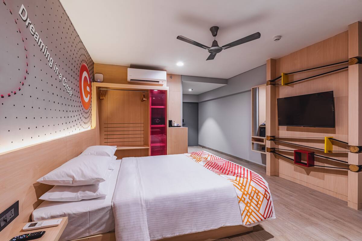 A modern hotel room with a bed, a TV, a ceiling fan, and a wardrobe.