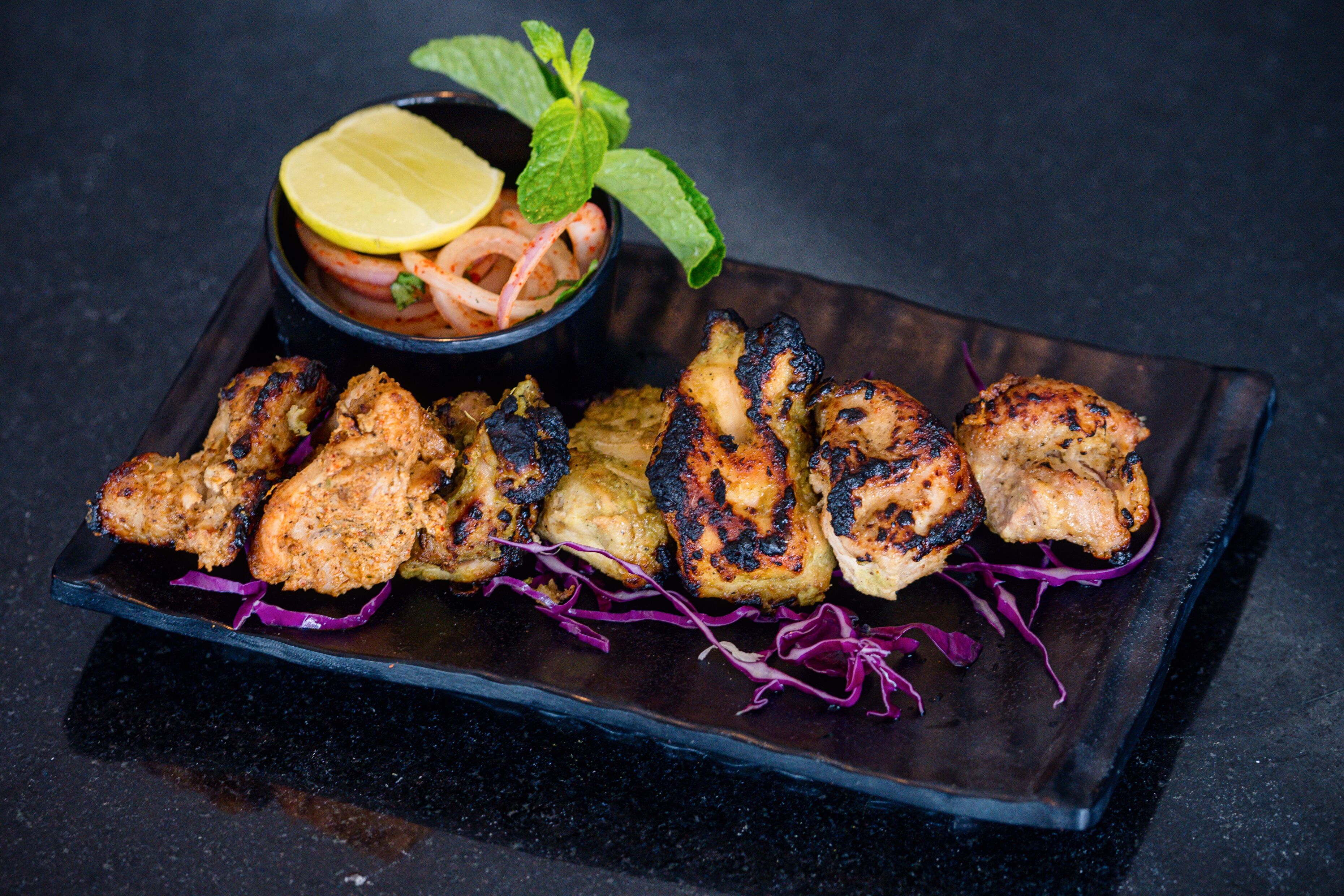 A plate of grilled chicken skewers with a side of onion salad and lemon slices.