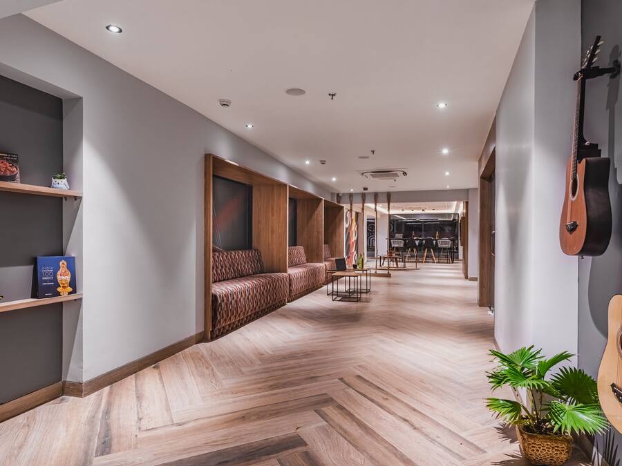 Un pasillo moderno de hotel con suelo de madera, asientos integrados y guitarras colgadas en la pared.