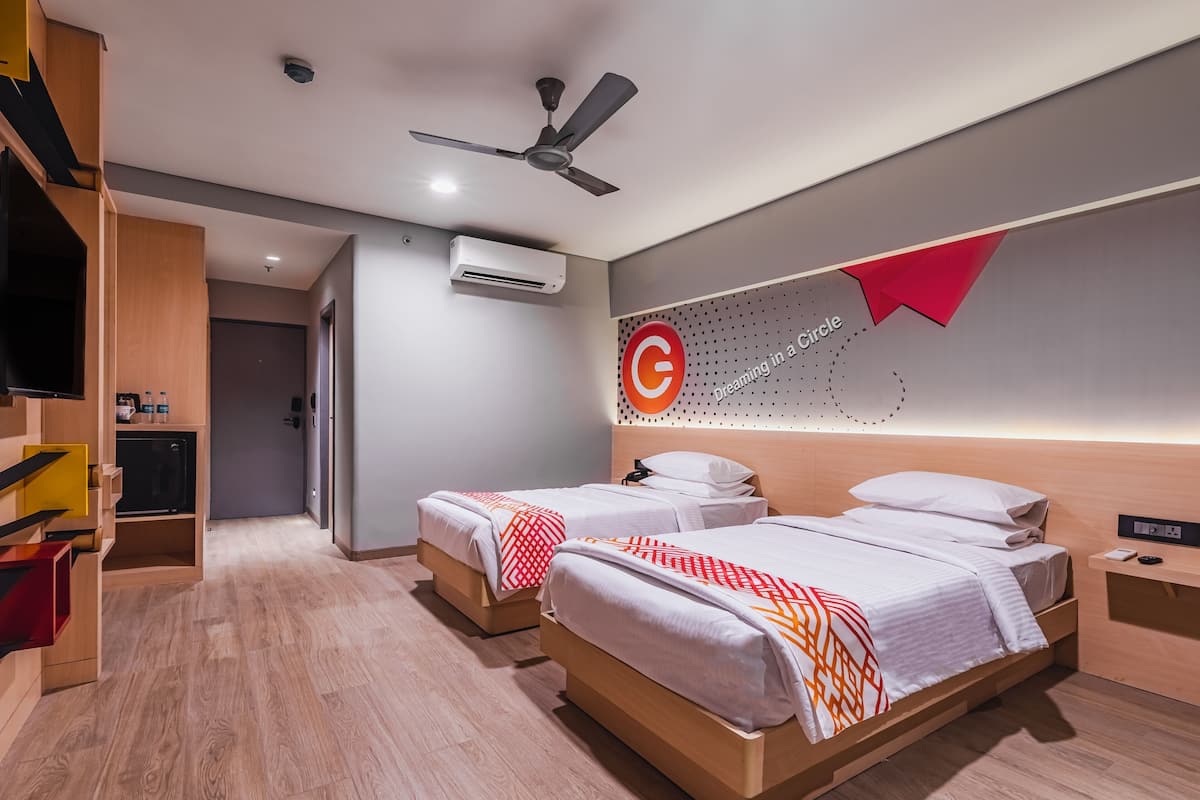 A hotel room with two beds, a ceiling fan, an air conditioning unit, a TV, and a wall-mounted light.