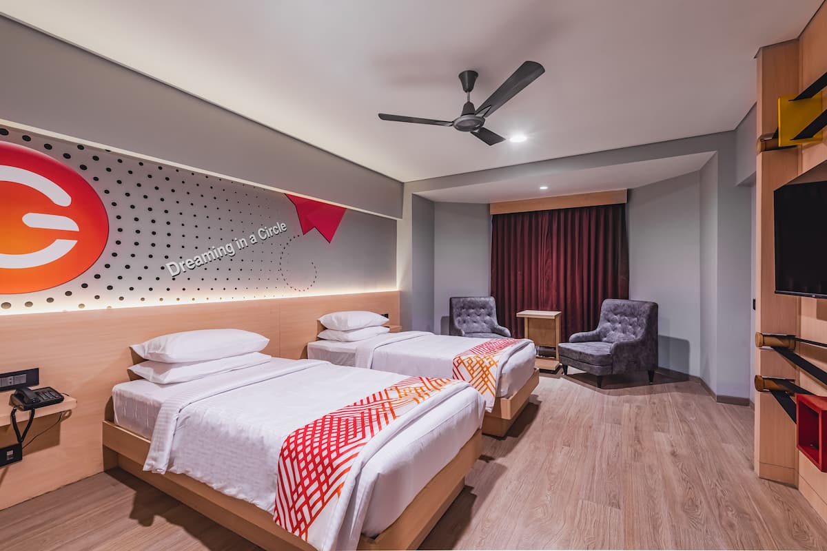 A hotel room with two beds, a ceiling fan, a TV, and a red curtain.