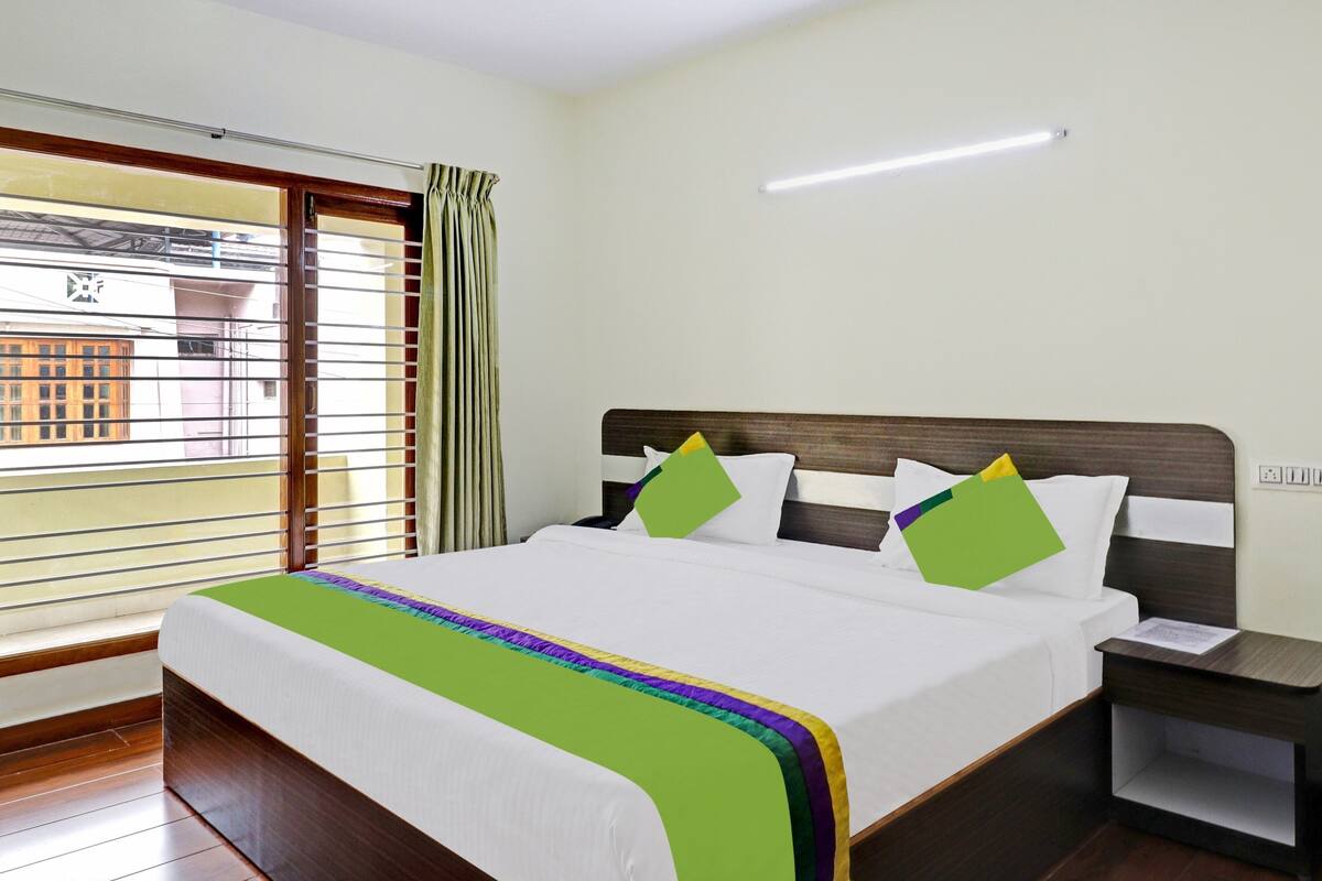 Hotelkamer met een bed, nachtkastje, raam met zonwering en uitzicht op gebouwen.