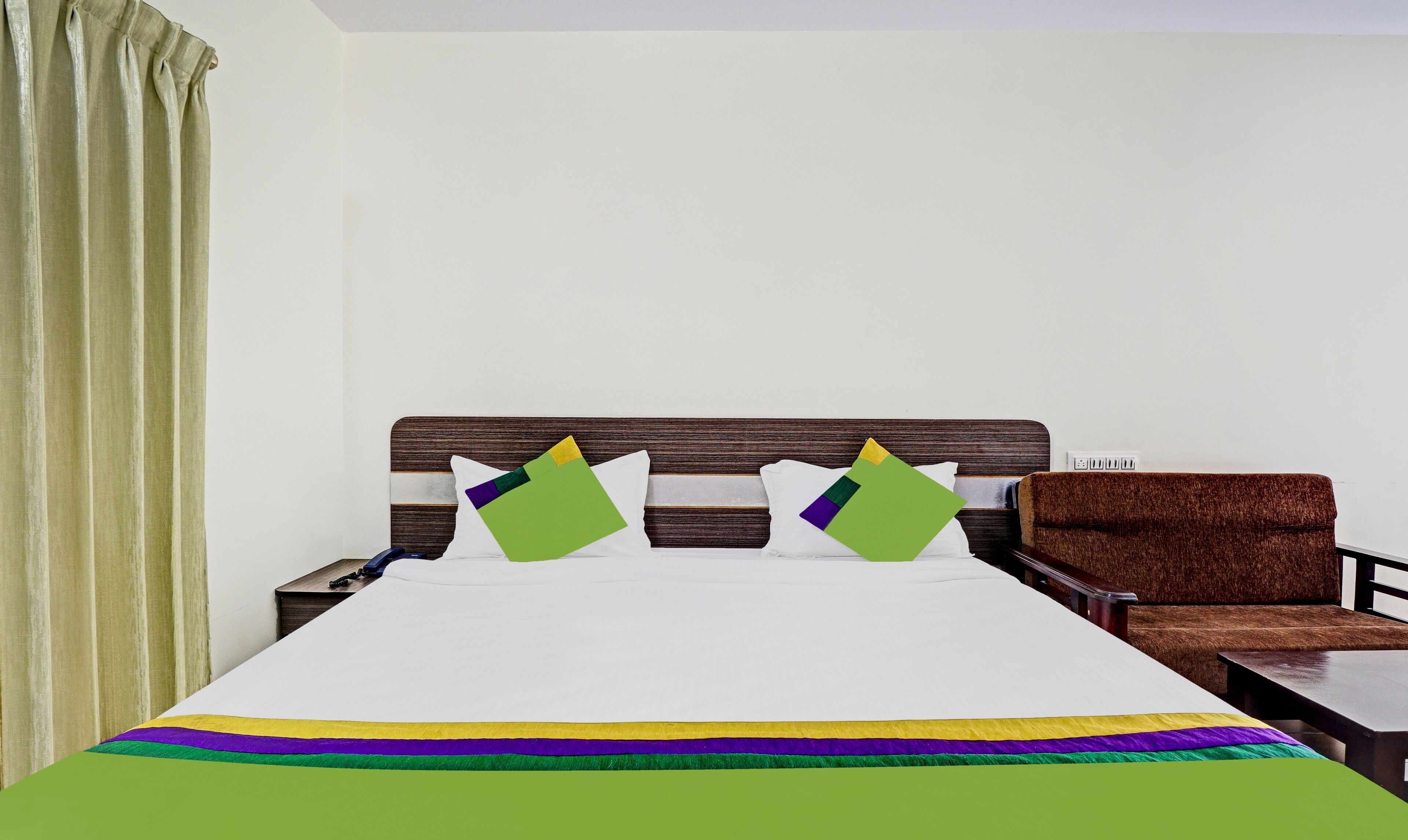 A hotel room with a large bed, two pillows, a wooden headboard, a brown armchair, and a small table.
