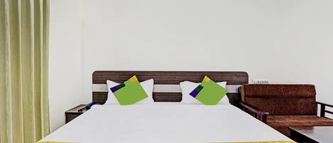 A hotel room with a large bed, two pillows, a wooden headboard, a brown armchair, and a small table.