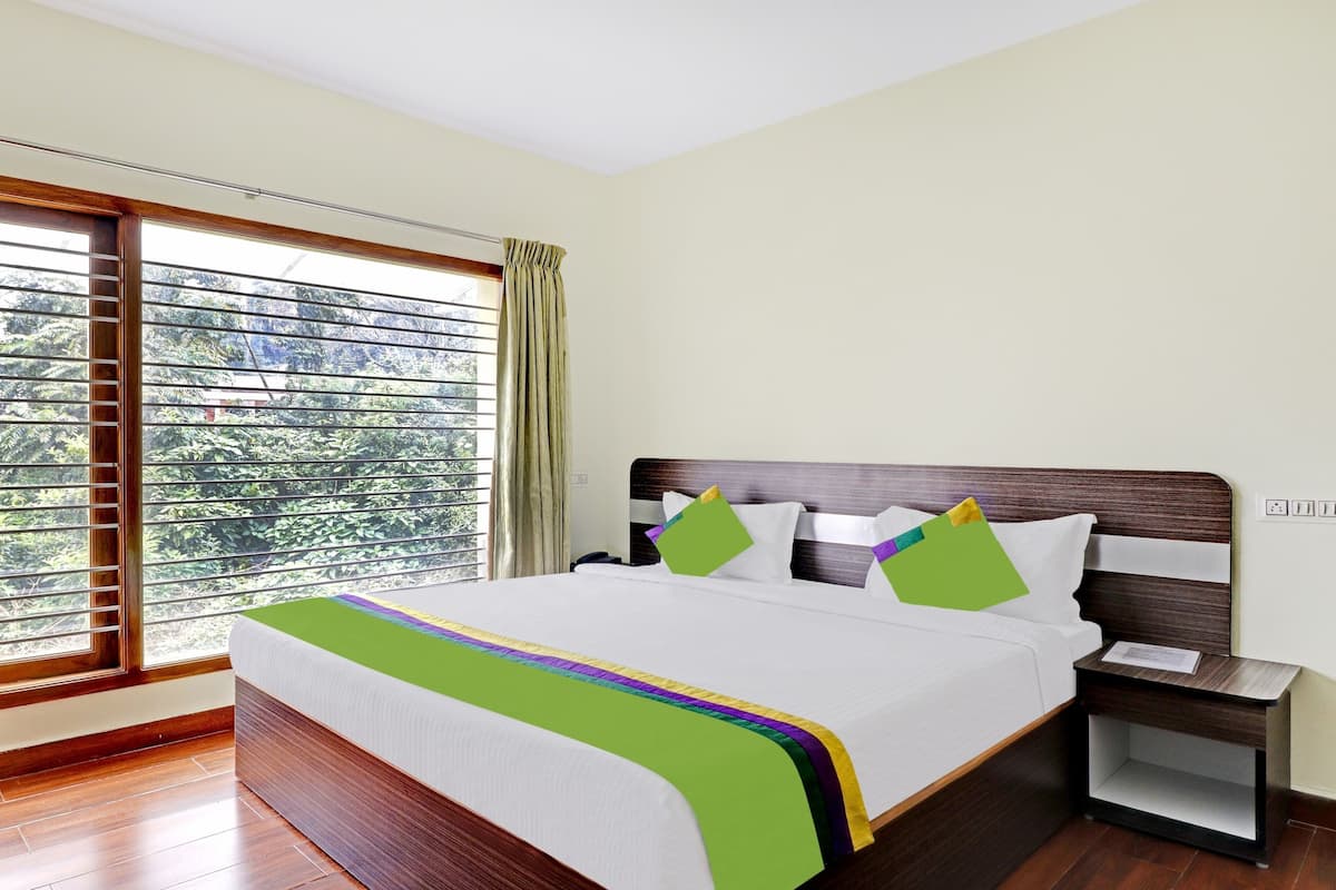 Een hotelkamer met een groot bed, nachtkastje en een raam met gordijnen.