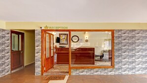 Zona de recepción con pared de mármol, mostrador de madera y un reloj.