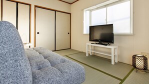 A room with tatami flooring, a sofa, a TV on a stand, and sliding doors.