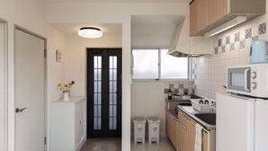 A modern kitchen with white cabinets, a microwave, and a sink. There is a small window above the sink and a door with frosted glass panels.