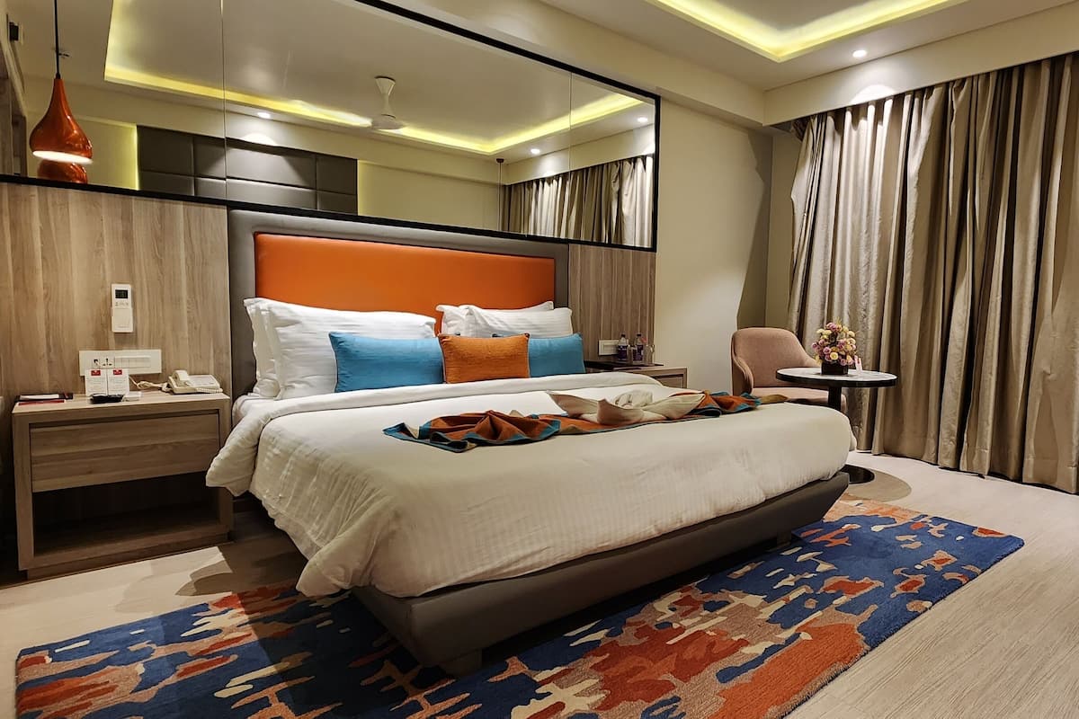 A modern hotel room with a large bed, a bedside table, a desk, and a chair.