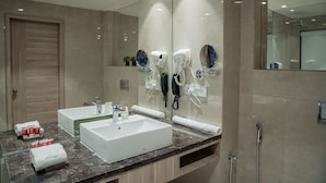 A modern bathroom with two sinks, a large mirror, and hair dryers mounted on the wall.