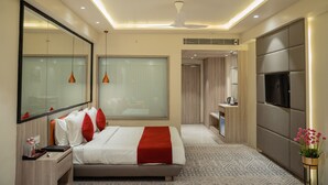 A modern hotel room with a large bed, a TV, a mirror, and a bathroom visible through a glass door.