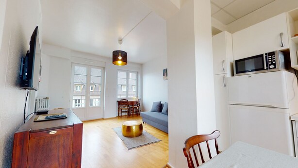 Ein gemütlicher, kleiner Wohnraum mit einem Holzschrank, einem Fernseher, einer Essecke mit Tisch und Stühlen, einer Couch und einer Küchenzeile mit Mikrowelle und Kühlschrank.