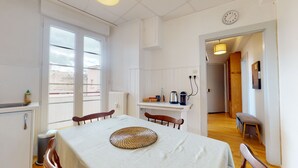 Ein Zimmer mit Esstisch, Stühlen, Heizkörper, Fenster, einer Uhr und einer Tür zu einem weiteren Raum.