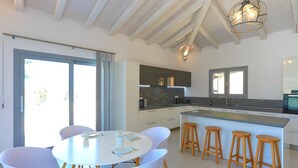 A modern kitchen with white cabinetry, a central island with stools, and a dining area with a round table and chairs. - Villa Loki in Kremithas (Corfu)