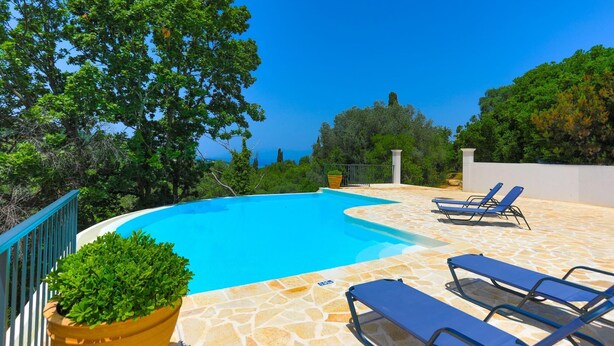 A swimming pool with lounge chairs, surrounded by stone flooring and greenery. - Villa Loki in Kremithas (Corfu)