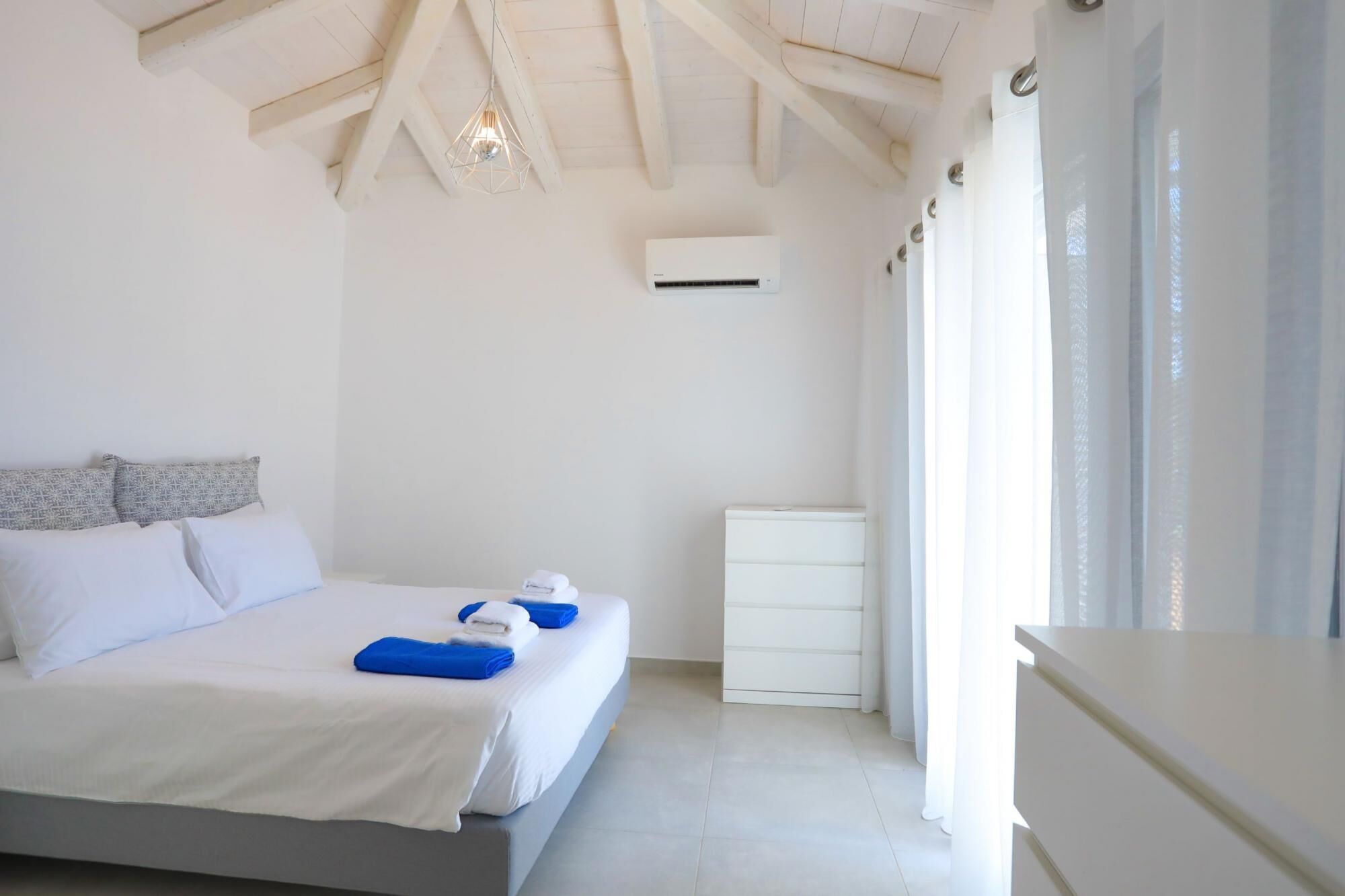 Una camera da letto con un letto, cuscini, un comodino, una cassettiera e una finestra con tende.