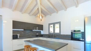 A modern kitchen with a large island, white cabinetry, and a built-in oven. - Villa Loki in Kremithas (Corfu)