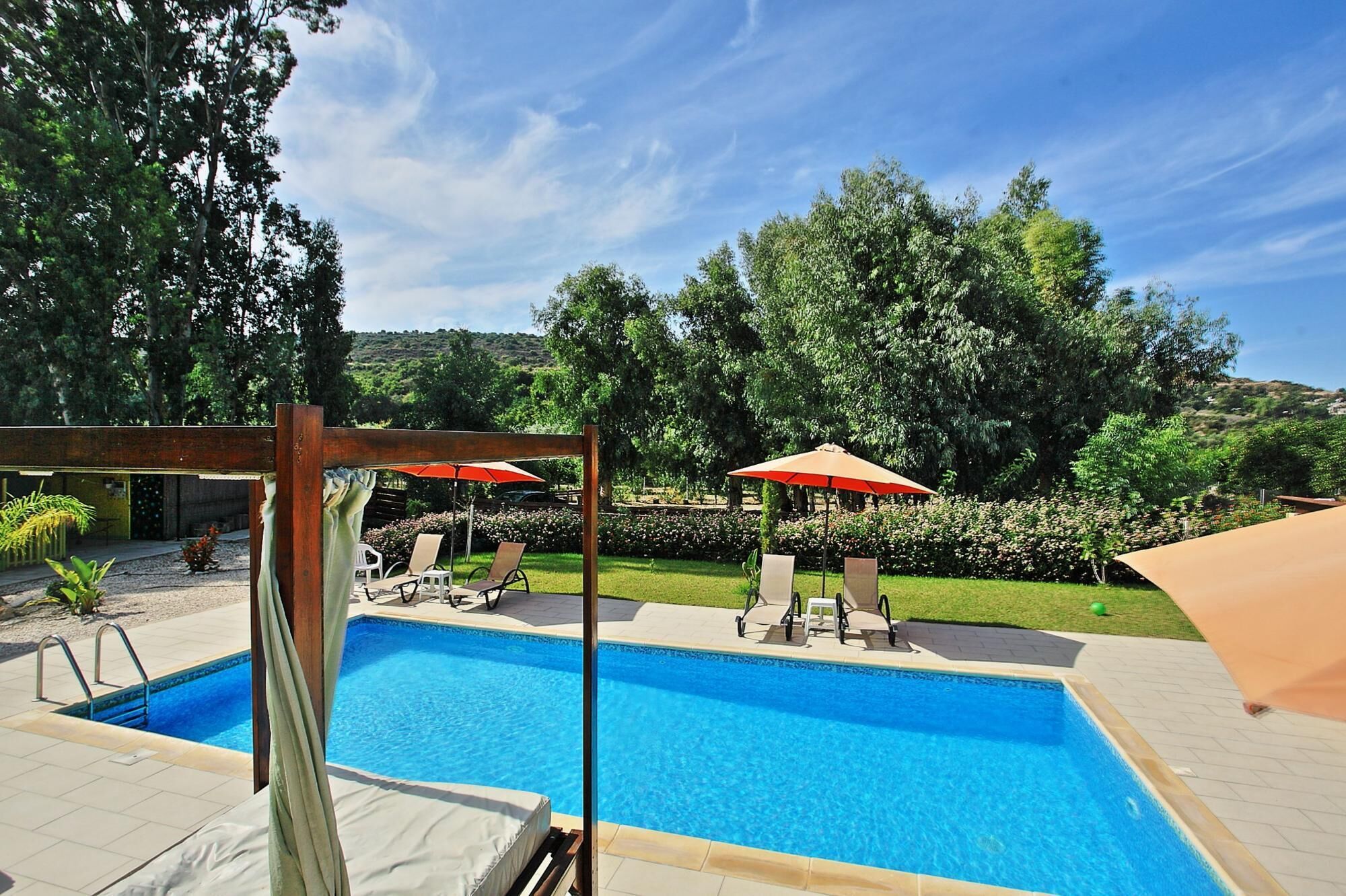 Une piscine entourée de verdure et agrémentée d’une pergola, avec des chaises longues et des parasols.