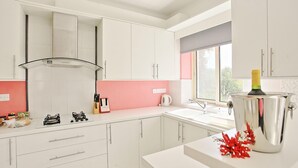 A modern kitchen with white cabinets, a pink backsplash, and a window providing natural light. - Villa Georgios Rafaela (Goudi)