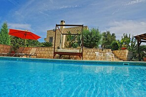 A swimming pool with a stone structure, lounge chairs, and an umbrella. - Villa Georgios Rafaela (Goudi)